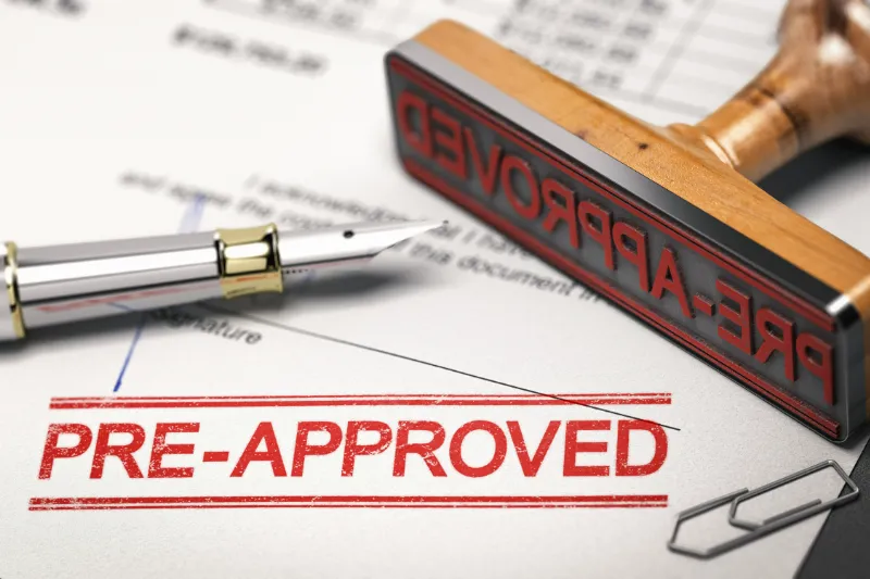 A fountain pen, paperclips, and a rubber stamp labeled PRE-APPROVED rest on paperwork, with a bold red PRE-APPROVED stamp marking the document.
