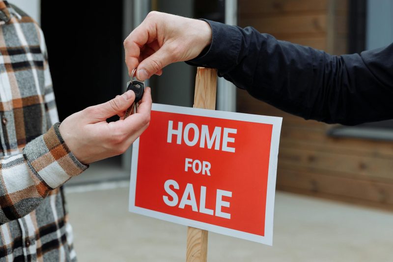 Blog 11 Closeup of a home for sale sign with people exchanging keys