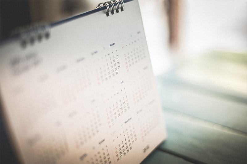 Learning Center 22 A close-up of a desk calendar displaying multiple months, with dates slightly blurred. The calendar rests on a wooden surface in soft, natural light.