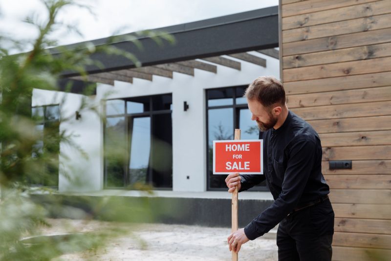 Home 25 man placing a home for sale sign outside a modern house