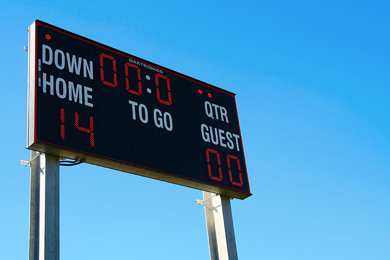 Home 186 A football scoreboard displays Home: 14, Guest: 0 with 0:00 time remaining, under a clear blue sky.