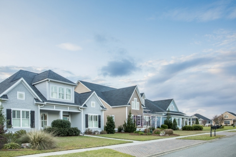 Home 151 A row of modern suburban houses with well-kept lawns and landscaping under a partly cloudy sky, lining a quiet residential street.