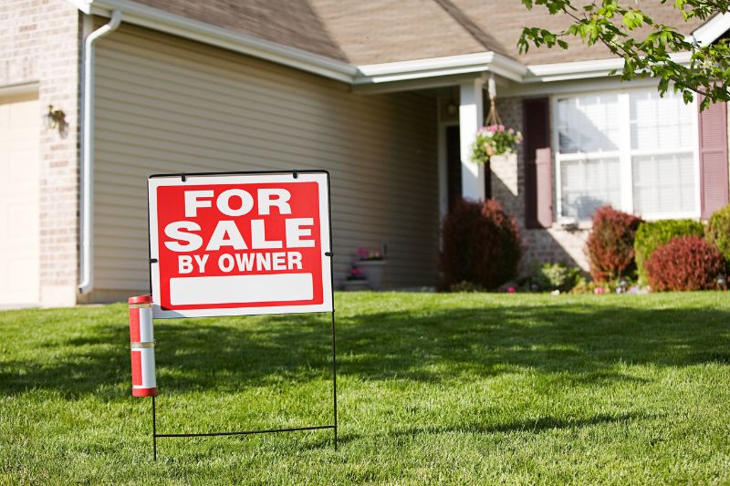 Home 141 A For Sale by Owner sign is displayed on the front lawn of a suburban house with beige siding, white trim, and maroon shutters on a sunny day.