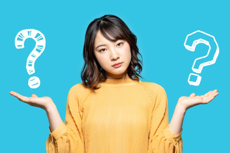 Home 38 A woman in a yellow top stands against a blue background, holding her hands up with a questioning expression. Large white question marks are illustrated near each hand, symbolizing confusion or decision-making.