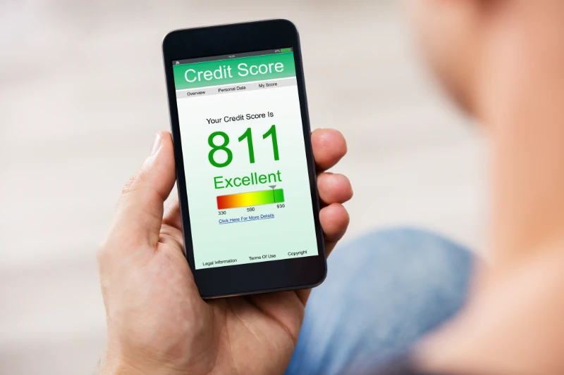 Home 24 A person holds a smartphone displaying a credit score of 811, labeled as Excellent, on a green-themed screen with a score range and navigation tabs visible at the top.