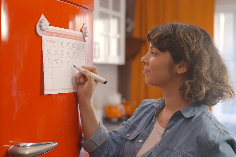 Blog 6 Woman marking off her calendar hanging on a fridge